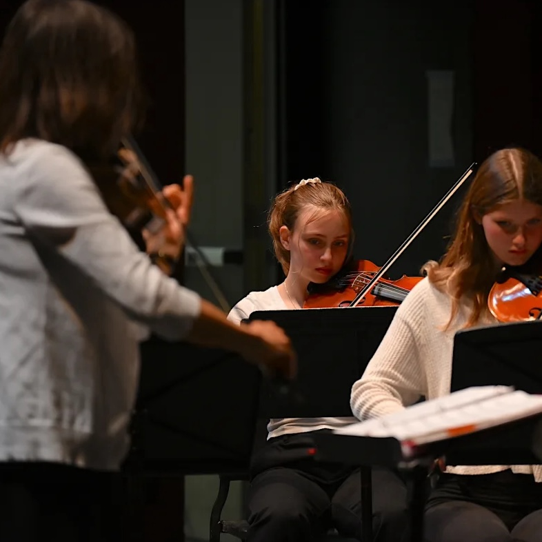 Ms Kost playing violin at concert with students