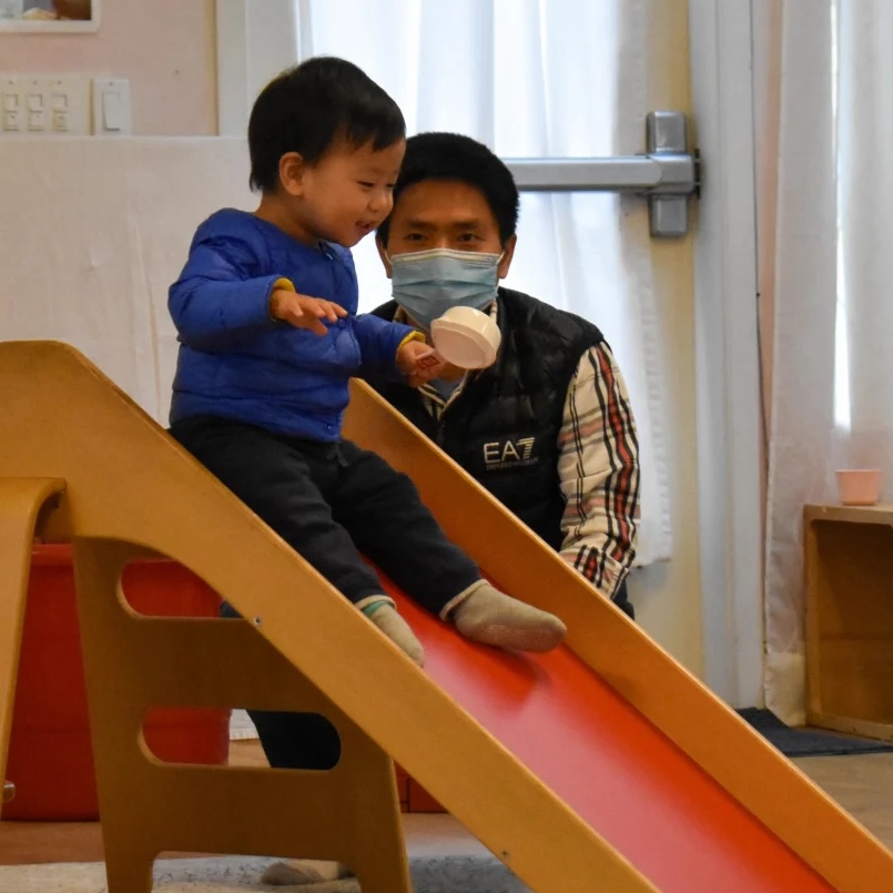 Parent child class. Dad watching baby go down slide.